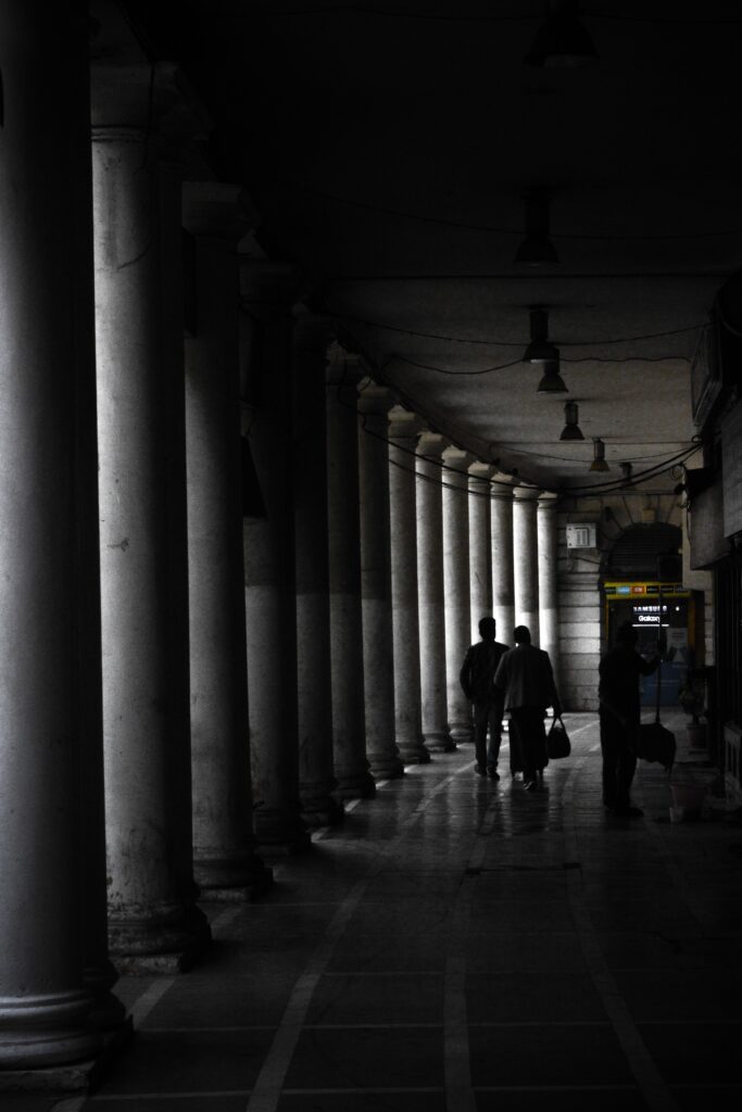 People walking through the iconic shaded corridor of Connaught Place, Delhi, creating a striking silhouette effect.